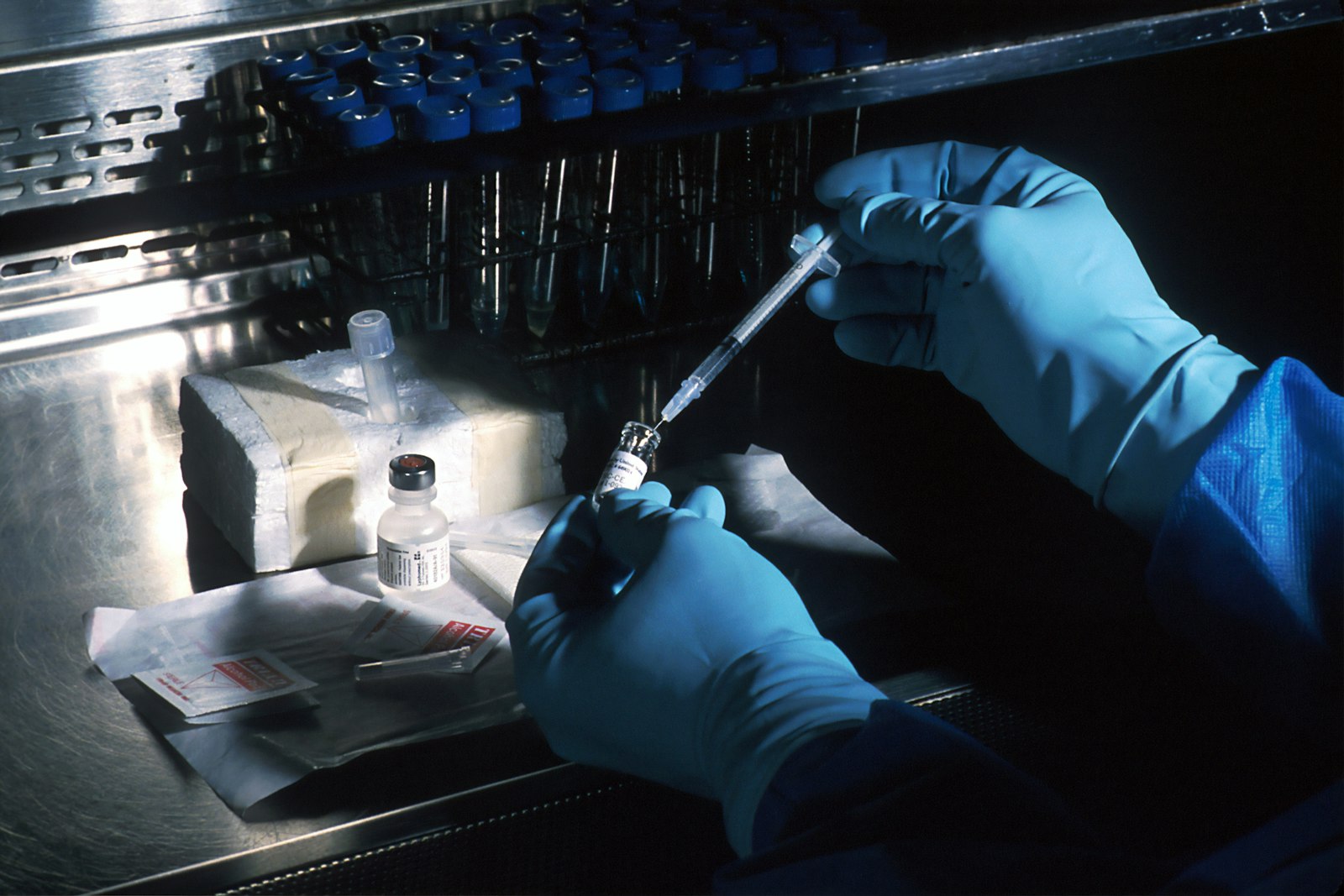 Gloved hands preparing a vial and syringe at a laboratory bench, representing ISO 15189 Ready laboratory training